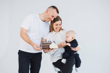 Mutlu bir aile çifti, kucağında küçük bir oğlu ve beyaz arka planda tatlı bir pastası var. Beyaz bir geçmişi olan genç bir aile..