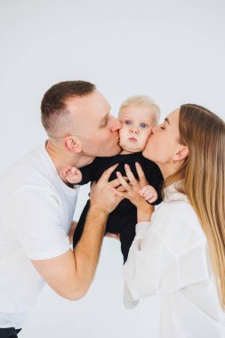 Genç ebeveynler, bir erkek ve bir kadın, küçük oğullarını öperler. Beyaz bir arka planda kollarında çocuğu olan bir aile çifti..