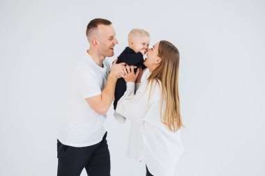 Genç ebeveynler, bir erkek ve bir kadın, küçük oğullarını öperler. Beyaz bir arka planda kollarında çocuğu olan bir aile çifti..