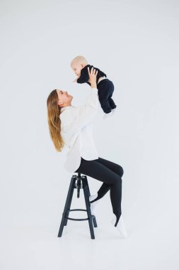 Genç bir anne beyaz arka planda oturur, bebeğini kollarına alır ve onu öper. Anne ve küçük oğlu..