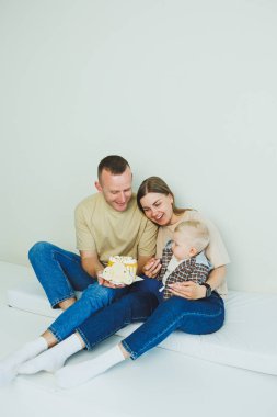 Kollarında bebek olan genç bir aile ellerinde pastayla oturuyor. Evli bir çift oğullarının doğum gününü kutluyor..