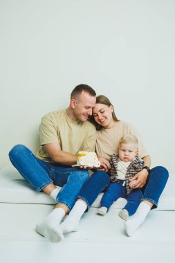 Kollarında bebek olan genç bir aile ellerinde pastayla oturuyor. Evli bir çift oğullarının doğum gününü kutluyor..