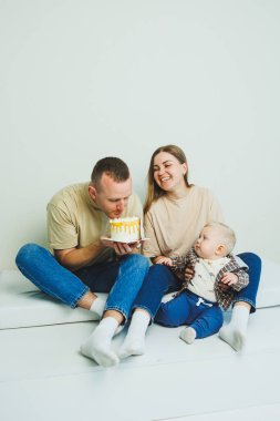 Kollarında bebek olan genç bir aile ellerinde pastayla oturuyor. Evli bir çift oğullarının doğum gününü kutluyor..