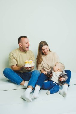 Kollarında bebek olan genç bir aile ellerinde pastayla oturuyor. Evli bir çift oğullarının doğum gününü kutluyor..