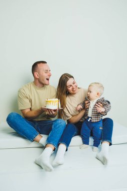 Kollarında bebek olan genç bir aile ellerinde pastayla oturuyor. Evli bir çift oğullarının doğum gününü kutluyor..