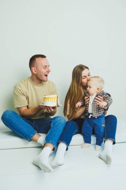 Kollarında bebek olan genç bir aile ellerinde pastayla oturuyor. Evli bir çift oğullarının doğum gününü kutluyor..