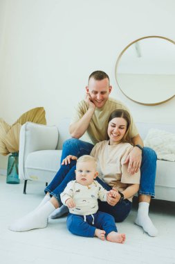 Genç ebeveynler 10 aylık oğullarıyla oynuyorlar. Annem ve babam evde bebekleriyle oynuyorlar. Ebeveynler çocuğa yürümeyi öğretir..