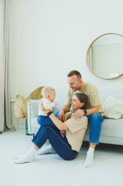 Genç ebeveynler 10 aylık oğullarıyla oynuyorlar. Annem ve babam evde bebekleriyle oynuyorlar. Ebeveynler çocuğa yürümeyi öğretir..