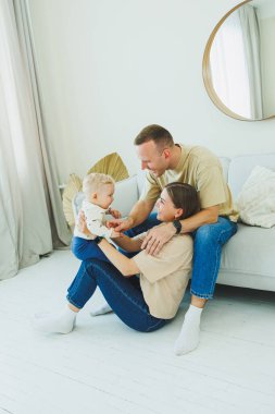 Genç ebeveynler 10 aylık oğullarıyla oynuyorlar. Annem ve babam evde bebekleriyle oynuyorlar. Ebeveynler çocuğa yürümeyi öğretir..