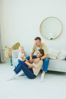 Genç ebeveynler 10 aylık oğullarıyla oynuyorlar. Annem ve babam evde bebekleriyle oynuyorlar. Ebeveynler çocuğa yürümeyi öğretir..