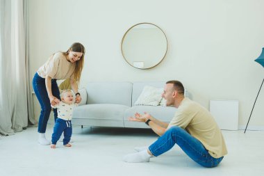 Genç evli bir çift modern bir oturma odasında küçük bir çocukla oynarken eğleniyor. Gülümseyen ebeveynler anne ve baba, evde sevimli, komik bir bebekle vakit geçirmekten zevk alıyorlar..