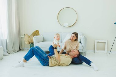Genç evli bir çift modern bir oturma odasında küçük bir çocukla oynarken eğleniyor. Gülümseyen ebeveynler anne ve baba, evde sevimli, komik bir bebekle vakit geçirmekten zevk alıyorlar..