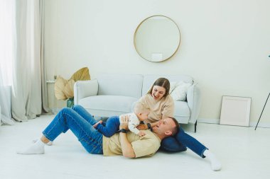 Genç evli bir çift modern bir oturma odasında küçük bir çocukla oynarken eğleniyor. Gülümseyen ebeveynler anne ve baba, evde sevimli, komik bir bebekle vakit geçirmekten zevk alıyorlar..