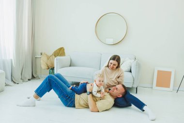 Genç evli bir çift modern bir oturma odasında küçük bir çocukla oynarken eğleniyor. Gülümseyen ebeveynler anne ve baba, evde sevimli, komik bir bebekle vakit geçirmekten zevk alıyorlar..