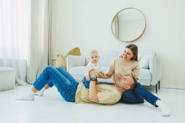 Genç evli bir çift modern bir oturma odasında küçük bir çocukla oynarken eğleniyor. Gülümseyen ebeveynler anne ve baba, evde sevimli, komik bir bebekle vakit geçirmekten zevk alıyorlar..