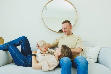 Genç evli bir çift modern bir oturma odasında küçük bir çocukla oynarken eğleniyor. Gülümseyen ebeveynler anne ve baba, evde sevimli, komik bir bebekle vakit geçirmekten zevk alıyorlar..