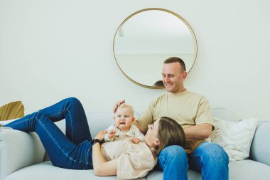 Genç evli bir çift modern bir oturma odasında küçük bir çocukla oynarken eğleniyor. Gülümseyen ebeveynler anne ve baba, evde sevimli, komik bir bebekle vakit geçirmekten zevk alıyorlar..