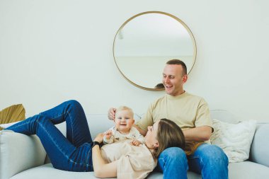 Genç evli bir çift modern bir oturma odasında küçük bir çocukla oynarken eğleniyor. Gülümseyen ebeveynler anne ve baba, evde sevimli, komik bir bebekle vakit geçirmekten zevk alıyorlar..