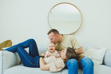 Genç evli bir çift modern bir oturma odasında küçük bir çocukla oynarken eğleniyor. Gülümseyen ebeveynler anne ve baba, evde sevimli, komik bir bebekle vakit geçirmekten zevk alıyorlar..