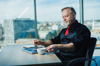 Erkek, gri saçlı, stil sahibi, dizüstü bilgisayarla çalışan, iş yerinde beyaz saçlı bir iş adamı. Ofiste sakallı bir patron var.