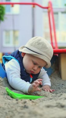 10 aylık küçük bir çocuk oyun parkındaki kum havuzunda oynuyor. Çocuk gelişimi. Çocuklar için kum oyunu
