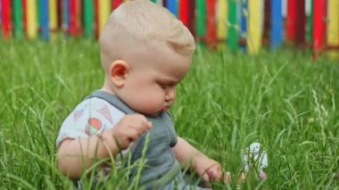 10 aylık bir erkek bebek çimlerin üzerinde otururken oynuyor. Doğada bir çocuk.
