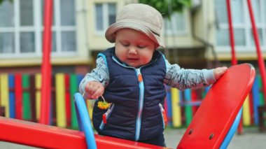 10 aylık bir erkek bebek sokakta durur ve bir desteğe tutunur, çocuk ayakta durmayı öğrenir. Bir çocuğun ilk adımları. Çocuğun kişisel gelişimi. Bebek kıyafetleri.