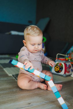 Pamuklu mayo giymiş bir erkek bebek halıya oturur ve eğitici oyuncaklarla oynar. Çocuğun kişisel gelişimi.