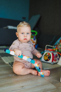Pamuklu mayo giymiş bir erkek bebek halıya oturur ve eğitici oyuncaklarla oynar. Çocuğun kişisel gelişimi.