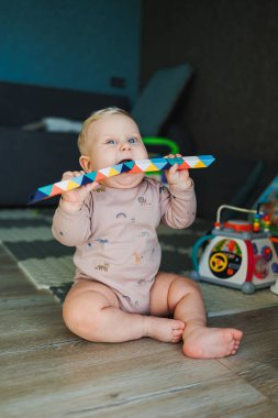 Pamuklu mayo giymiş bir erkek bebek halıya oturur ve eğitici oyuncaklarla oynar. Çocuğun kişisel gelişimi.