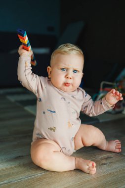 Pamuklu mayo giymiş bir erkek bebek halıya oturur ve eğitici oyuncaklarla oynar. Çocuğun kişisel gelişimi.