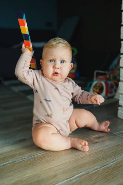 Pamuklu mayo giymiş bir erkek bebek halıya oturur ve eğitici oyuncaklarla oynar. Çocuğun kişisel gelişimi.