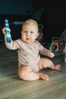 Küçük bir çocuk, takım elbiseli bir çocuk, parlak odada halı üzerinde oyuncaklarla oynuyor, mavi gözlü bir bebek.