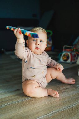 Küçük bir çocuk, takım elbiseli bir çocuk, parlak odada halı üzerinde oyuncaklarla oynuyor, mavi gözlü bir bebek.