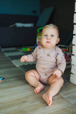Küçük bir çocuk, takım elbiseli bir çocuk, parlak odada halı üzerinde oyuncaklarla oynuyor, mavi gözlü bir bebek.