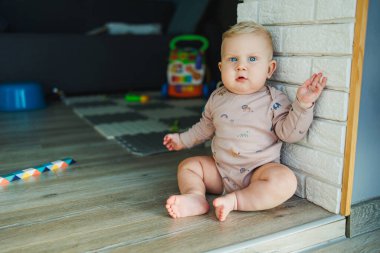Küçük bir çocuk, takım elbiseli bir çocuk, parlak odada halı üzerinde oyuncaklarla oynuyor, mavi gözlü bir bebek.