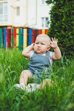Açık renk saçlı, tişörtlü bir çocuk çimenlerde otururken oynuyor. Çocuk gelişimi.