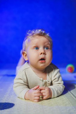 Küçük bir çocuk, takım elbiseli bir çocuk, parlak odada halı üzerinde oyuncaklarla oynuyor, mavi gözlü bir bebek.