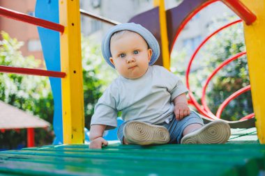 Sarışın, mavi gözlü bir çocuk, 11 aylık bir bebek, oyun parkında oynuyor. Yazlık elbiseli bir çocuk..