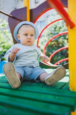 Sarışın, mavi gözlü bir çocuk, 11 aylık bir bebek, oyun parkında oynuyor. Yazlık elbiseli bir çocuk..