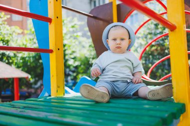 Sarışın, mavi gözlü bir çocuk, 11 aylık bir bebek, oyun parkında oynuyor. Yazlık elbiseli bir çocuk..