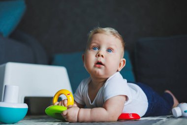 Beyaz elbiseli bir erkek bebek evde bir halıya oturup plastik bir piramitle oynuyor. Bebekler için eğitici oyunlar