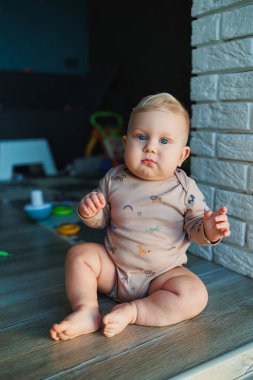 Açık renk saçlı, mavi gözlü bir çocuk. Bebek, 11 ay boyunca mayoyla evde oturuyor ve gülümsüyor. Çocuklar evde oynuyorlar..