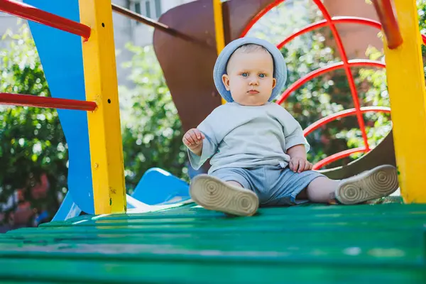 Sarışın, mavi gözlü bir çocuk, 11 aylık bir bebek, oyun parkında oynuyor. Yazlık elbiseli bir çocuk..