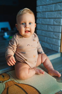 Açık renk saçlı, mavi gözlü bir çocuk. Bebek, 11 ay boyunca mayoyla evde oturuyor ve gülümsüyor. Çocuklar evde oynuyorlar..