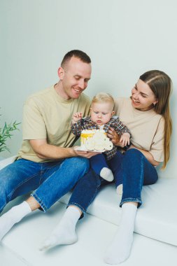 Mutlu ebeveynler küçük oğullarını kollarında tutarlar. Kollarında bir bebekle beyaz bir geçmişleri olan bir aile..