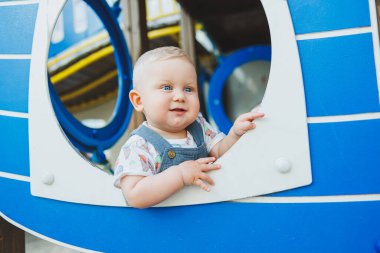 Mavi gözlü küçük bir çocuk güneşli bir yaz gününde oyun bahçesinde oynuyor. Çocuk yürümeyi öğreniyor..