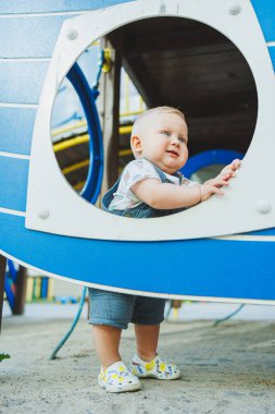 Mavi gözlü küçük bir çocuk güneşli bir yaz gününde oyun bahçesinde oynuyor. Çocuk yürümeyi öğreniyor..