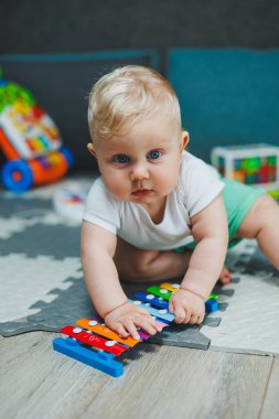 10 aylık sarı saçlı bir çocuk evde yerde oturup oyuncaklarla oynuyor. Bebekler için eğitici oyuncaklar. Çocuğun kişisel gelişimi.