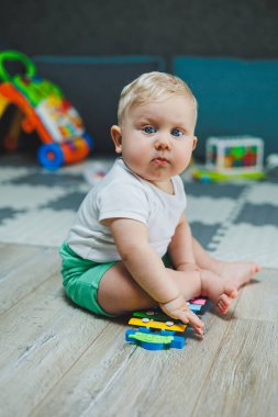 10 aylık sarı saçlı bir çocuk evde yerde oturup oyuncaklarla oynuyor. Bebekler için eğitici oyuncaklar. Çocuğun kişisel gelişimi.
